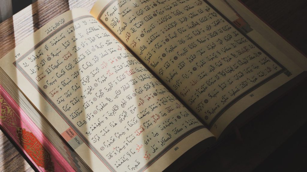 The Art of Drawing Readers In: Your attractive post title goes here An open Quran with Arabic script illuminated by natural sunlight on a wooden surface.